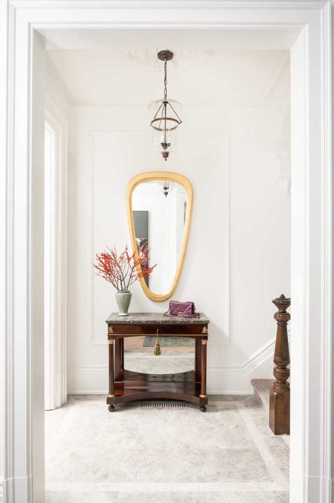 Foyer featuring a contemporary organic shaped mirror above a traditional piece of furniture in a white, light and airy space