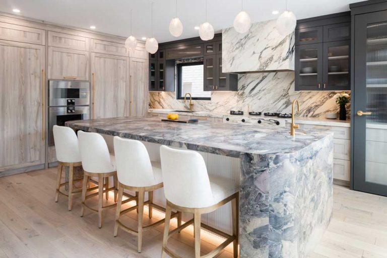 Kitchen island made of marble with four bar stools, kitchen in neutral colours in the background