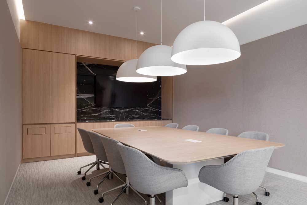 Conference room in a neutral pallete and wooden finishes with statement pendant lighting above the table.