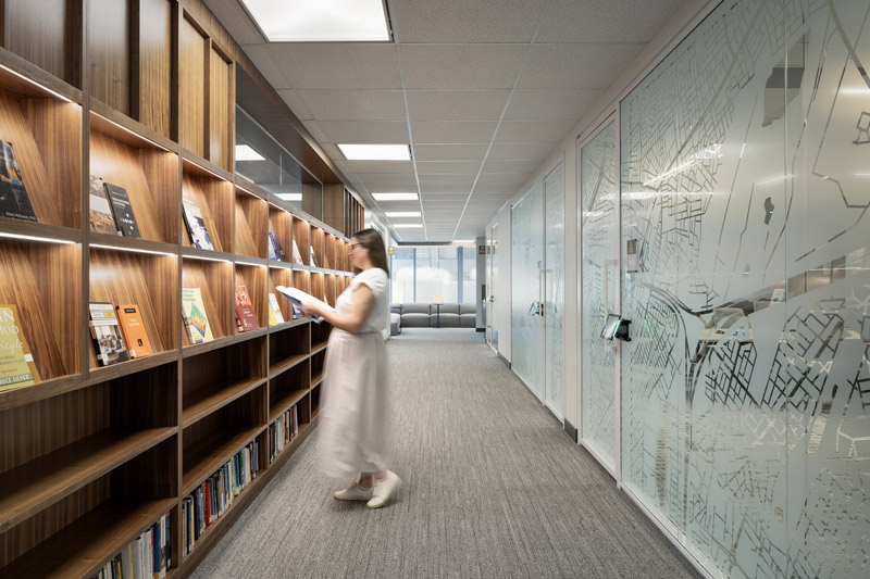 Custom millwork covers an entire wall in this hallway, while on the opposite side there are offices behind glass walls featuring a graphic of a city plan