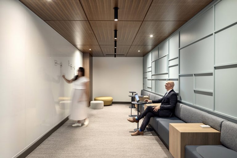 A collaborative space in the IRDC offices featuring a full white board wall on one side and on the other seating with a wall in a geometric pattern. The ceiling is covered in wood finish in a linear pattern