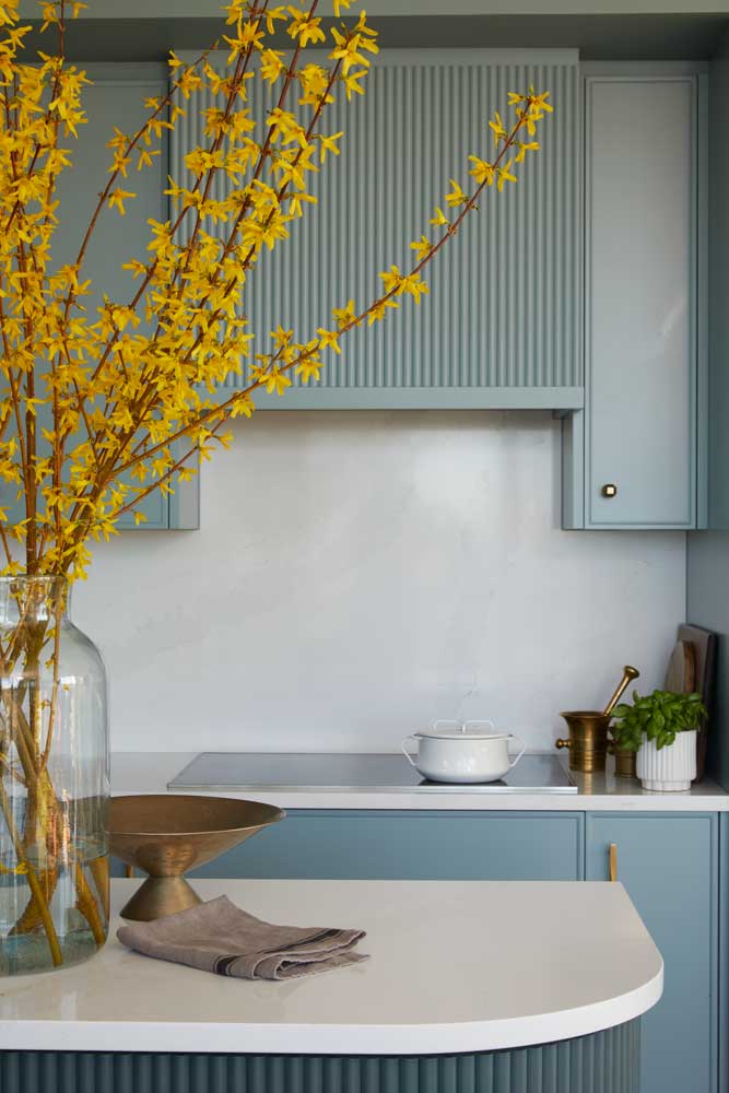 A vignette of the teal kitchen cabinets and contrasting yellow flowers on the island