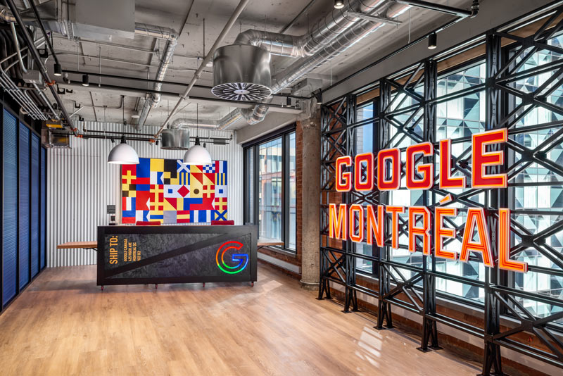 Google Montreal reception desk with colourful detail behind the desk and neon sign with company name against the industrial detailing on the windows