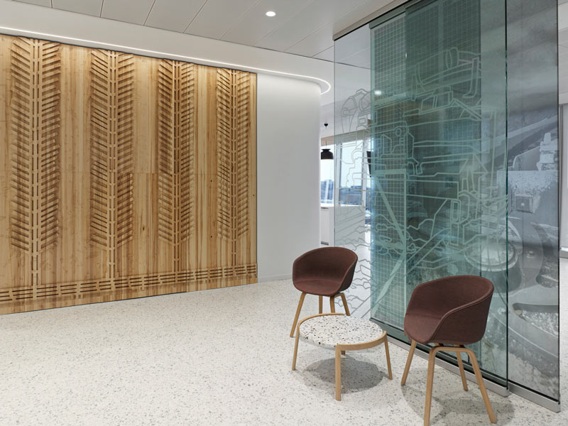 A small waiting area with earth toned chairs, wood elements and glass details on the wall resembling water