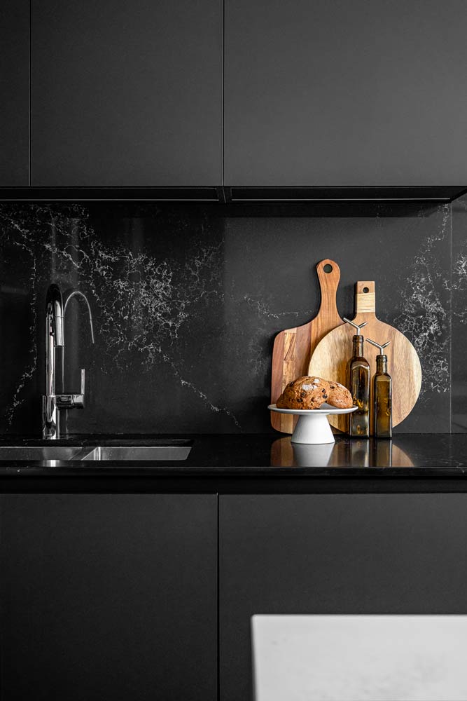 Black matte kitchen cabinets without hardware and matching black stone on counters and backsplash with contrasting wooden boards on the countertop