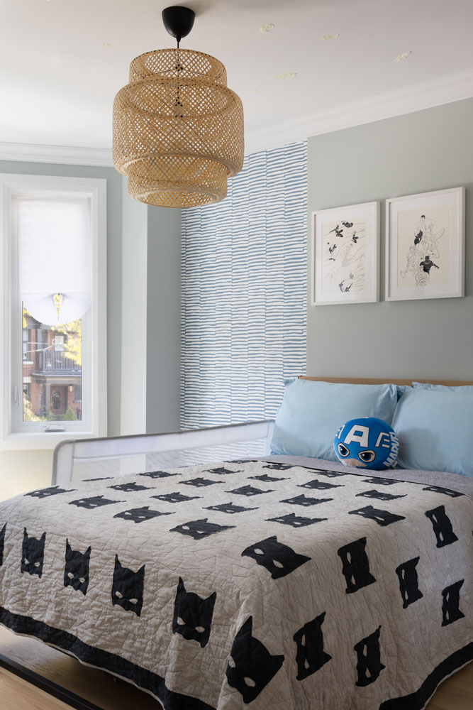 Kid's bedroom with a fun wall paper on one section of the wall and two pieces of art work above the bed. The light fixture that hangs above the bed is made of rattan