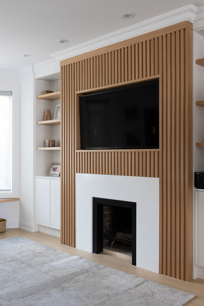 Fire place with the vertical wooden slat detail, and white flat surface encasing the opening of the fire place. Built-in shelving on both sides of the fireplace