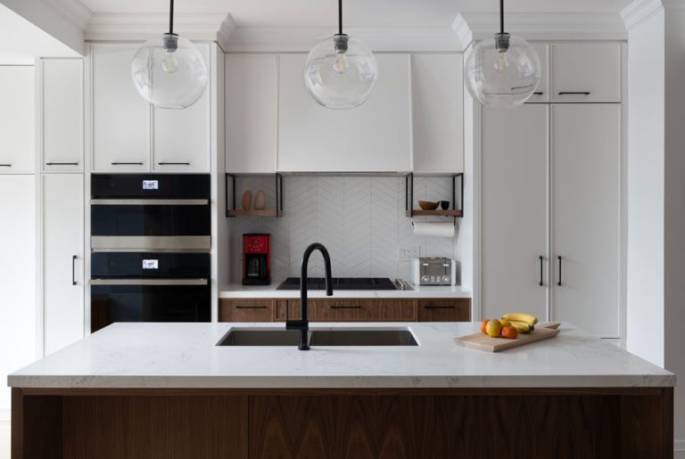 Kitchen is white with wood accents and industrial style lighting above the island