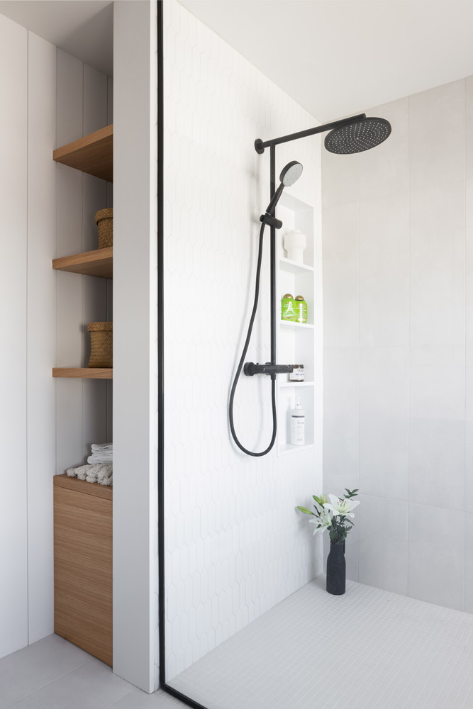 Main bathroom shower in white tile and black hardware, and beside it a narrow built in shelf