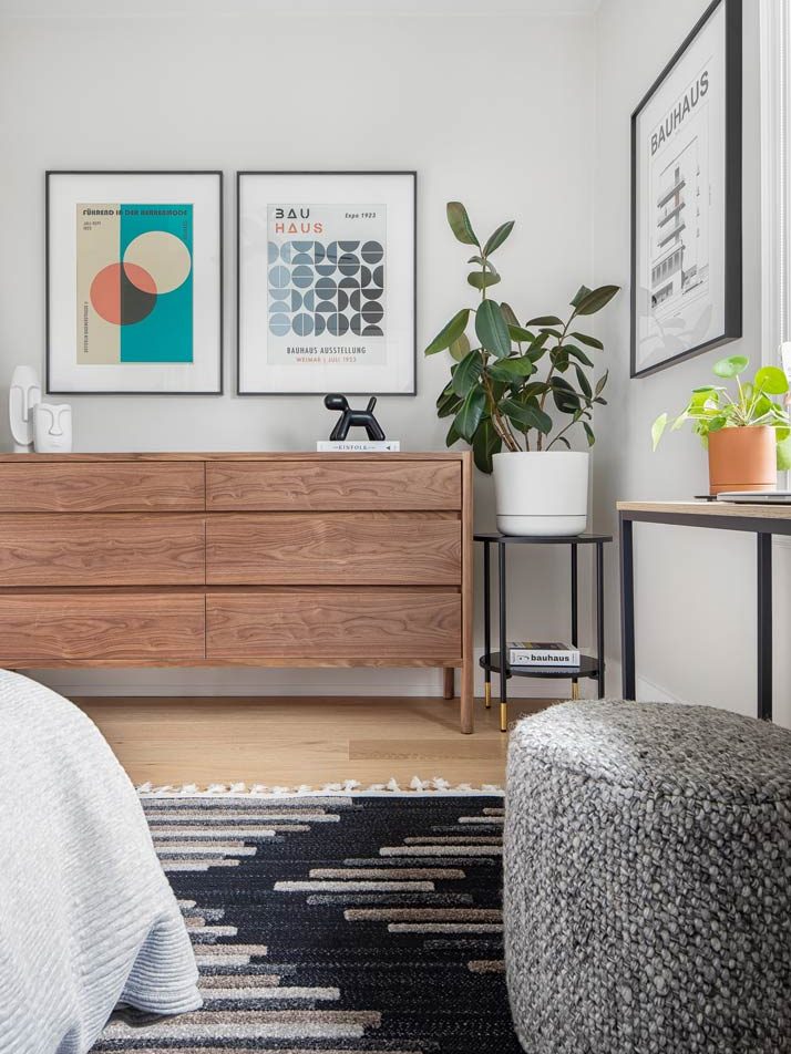 One of the kids' rooms in a clean mid century style with art posters on the wall and warm wooden furniture, a black and grey area rug