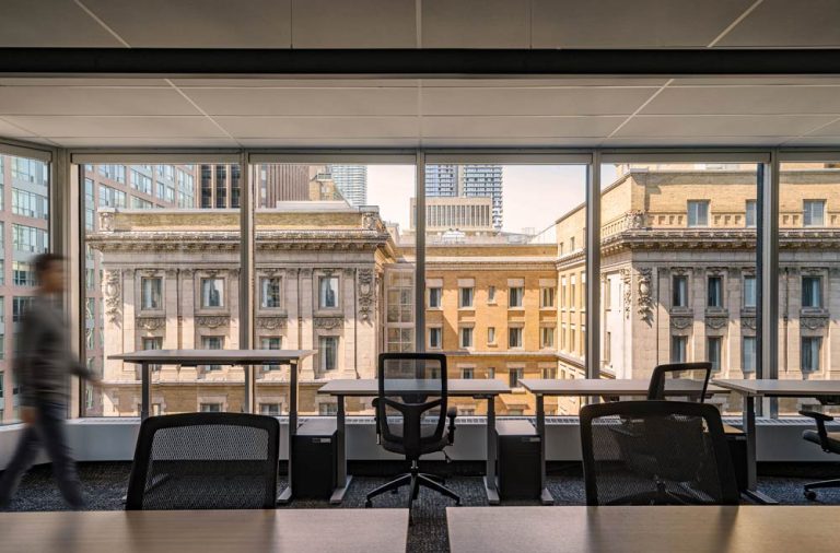 Working stations and tables lined against a floor to ceiling window looking onto the buildings across the street