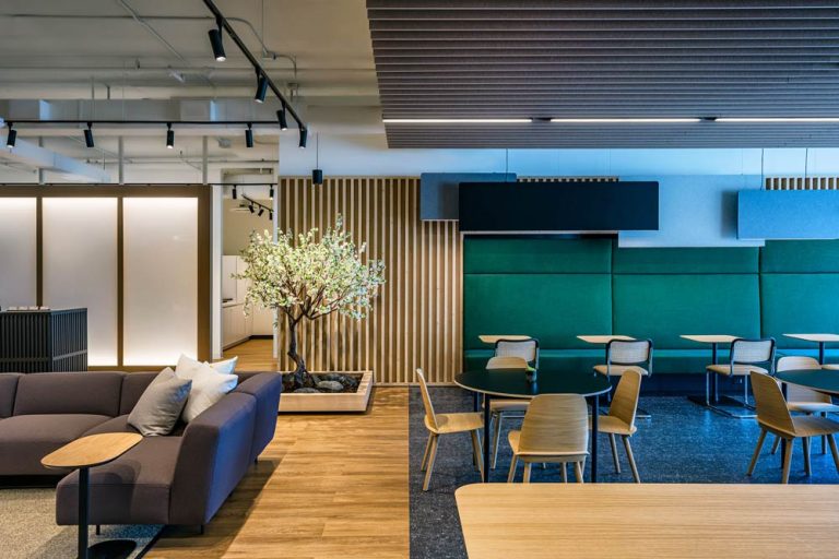 Adjacent to the reception area is the cafe area with tables and chairs, a lot of wooden finishes and contrasting dark green details on the wall