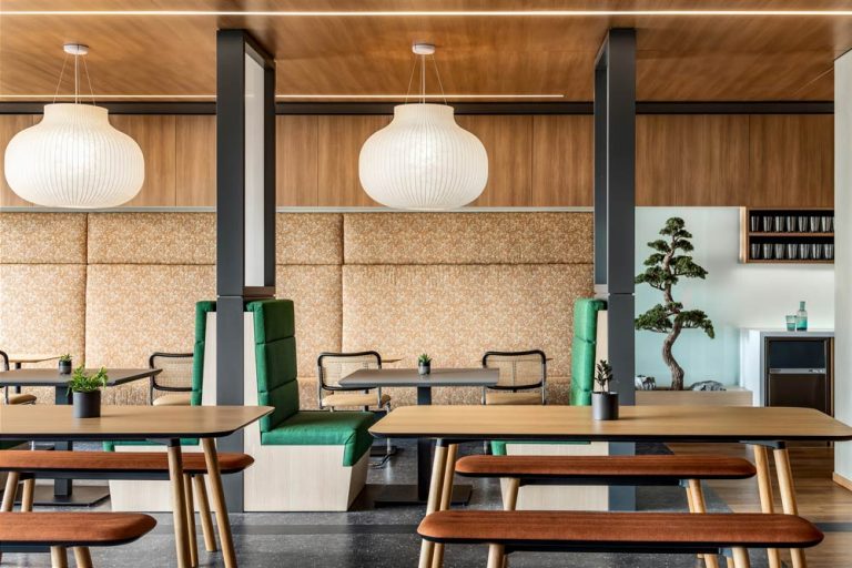 Booths in the cafe area adjacent to the bar and kitchen, with large paper lanterns above, bright green upholstered seating and patterned fabrics on the walls in a more subtle colour scheme.