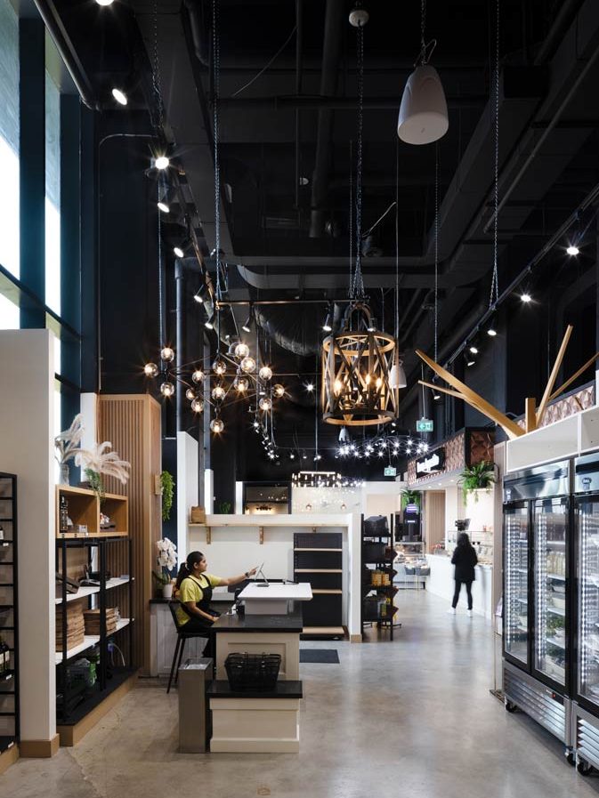 A view at the whole kitchen and market area showing industrial touches like lighting, black ceilings, fluted and metal shelves and concrete floors