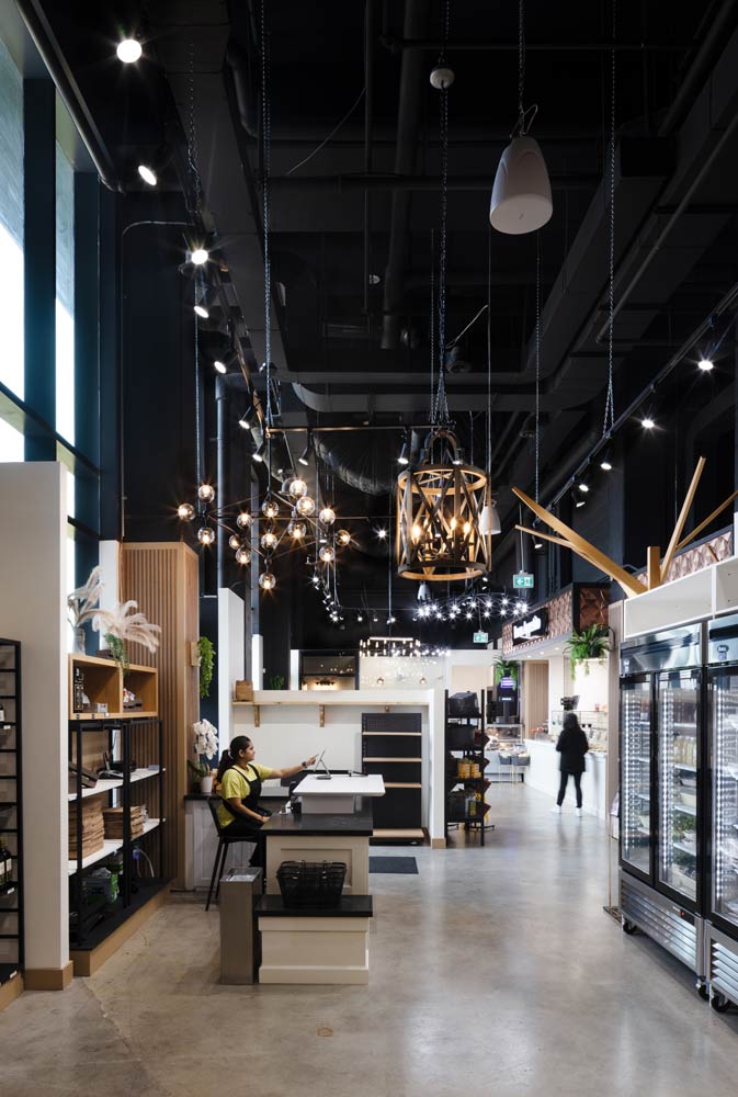 A view at the whole kitchen and market area showing industrial touches like lighting, black ceilings, fluted and metal shelves and concrete floors