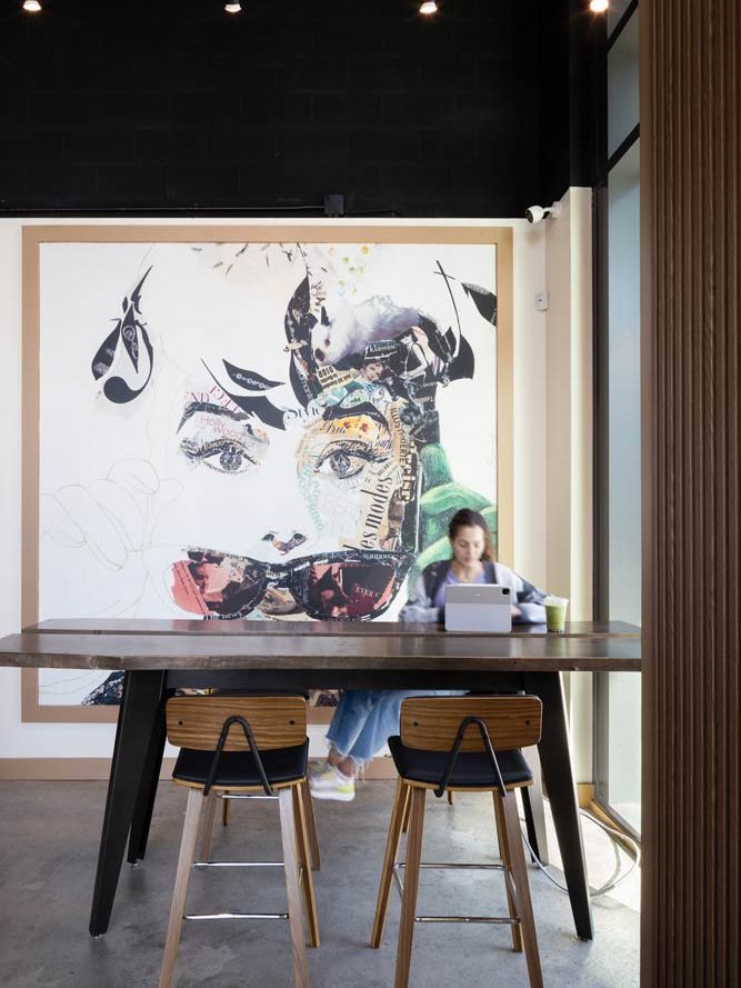 Large colourful mural like wall art of a woman's face behind a tall table with four industrial style chairs.