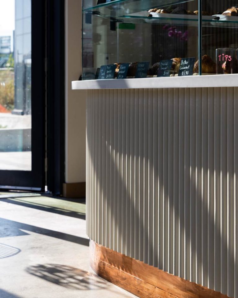 Fluted detail on the base of the counter in a neutral beige tone and window full of sweet pastries on top