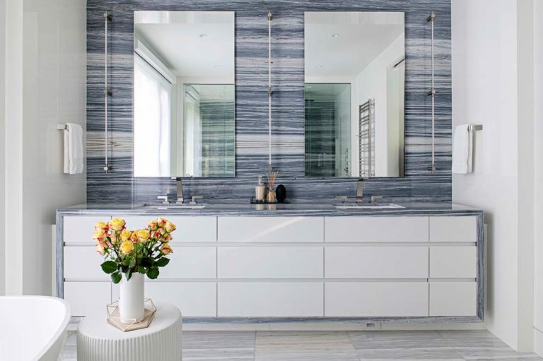 Principal bathroom featuring the wall hung vanity encased in a patterned marble that runs all the way up the wall behind the clean cut rectangular mirrors