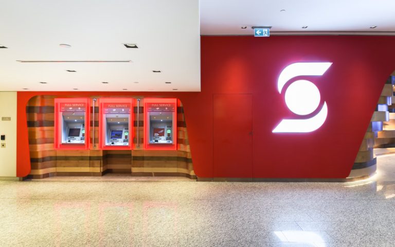 Around the corner from the main lounge area is a wall with red branded wall and next to it are three ATM machines