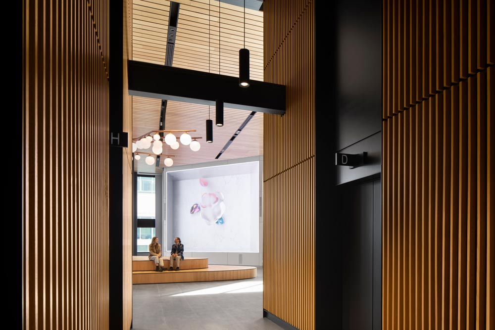 A view from the elevator lobby where the walls are covered in wood slats with black details like beams and hanging linear light fixtures