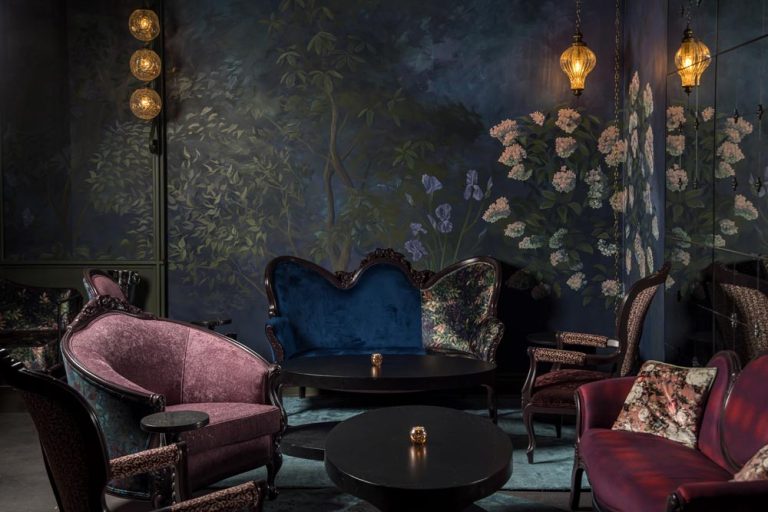 In this vintage lounge area there are beautiful murals on the walls, intricate lighting on the walls and colourful lounge seating