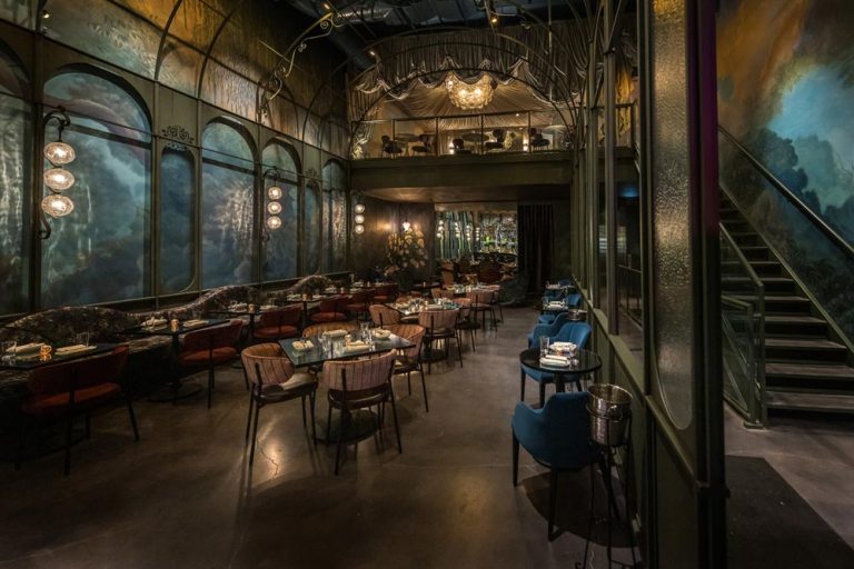 This main are of the restaurant shows custom whimsical murals framed by a custom Victorian greenhouse, a tent-draped mezzanine and a 2-story mirror installation