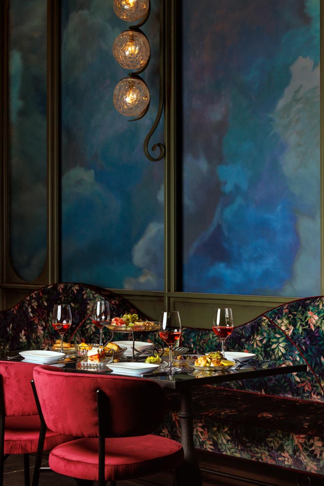 A vignette of a table and seating in the dining area, showing the colourful mural on the wall and custom lighting