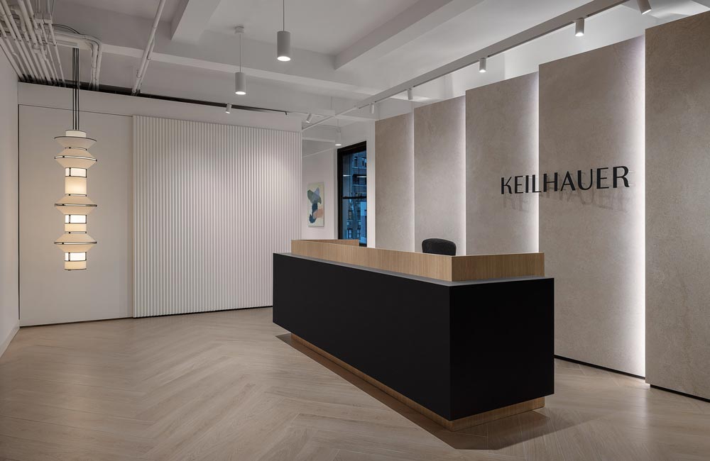 Dark brown reception desk at Keilhauer showroom with illuminated signage on a limestone wall featuring vertical thin lights