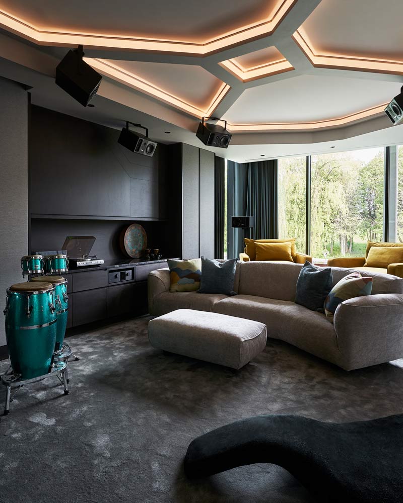 The comfy music room with comfortable couch for seating and a drum set. Interesting geometric lighting feature on the ceiling above and rounded large windows