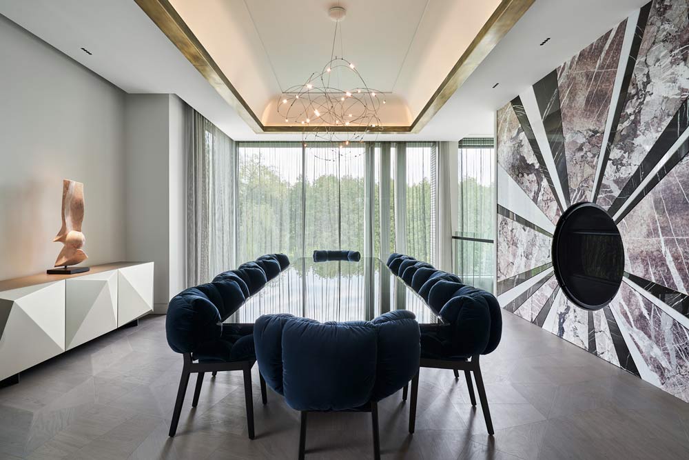 Dining room with the long dining table in the middle room and a large floor to ceiling windows at the other end of the room. The room features an exquisite fire place inspired by a rising sun on the wall on the right