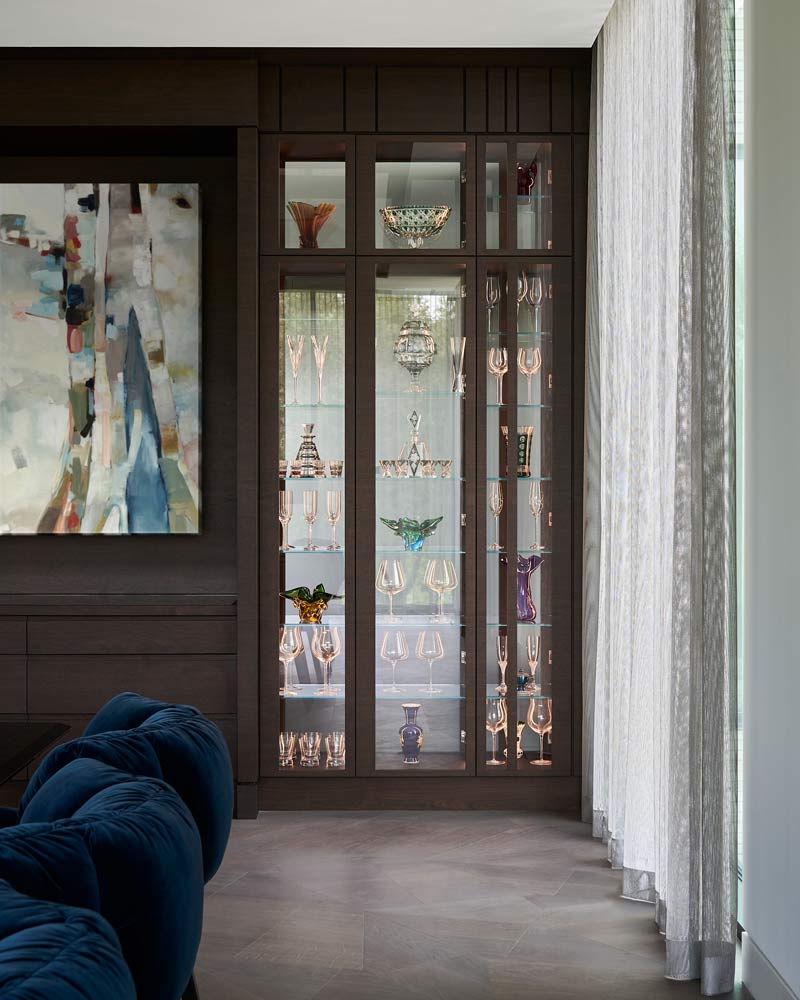 A built in shelving unit displaying glass items and dishes, and houses a colourful artwork on the wooden wall