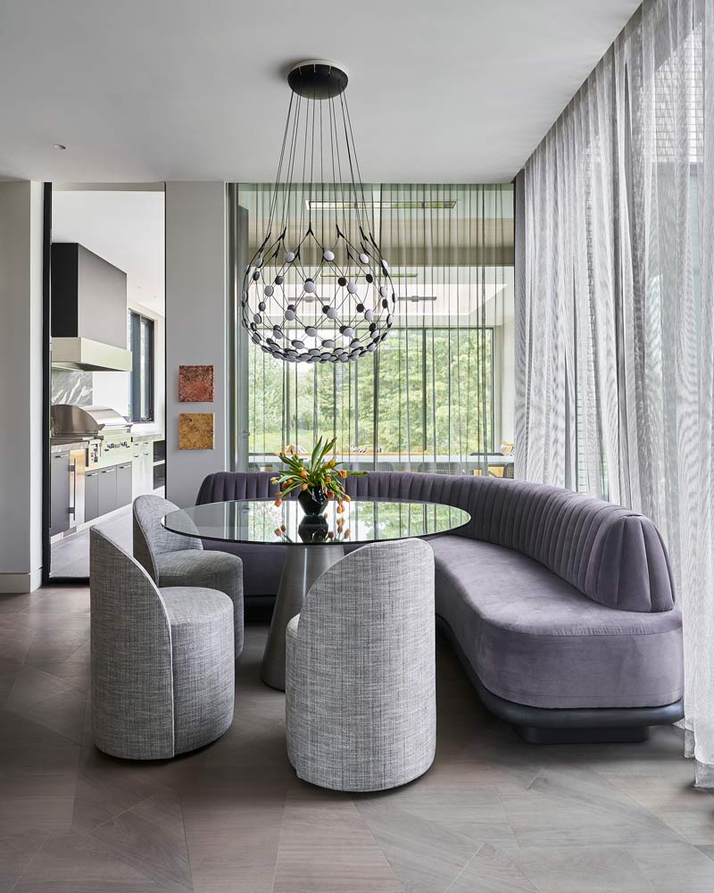 A quiet seating area with a rounded bench and three swivel chairs just outside the kitchen surrounded by windows