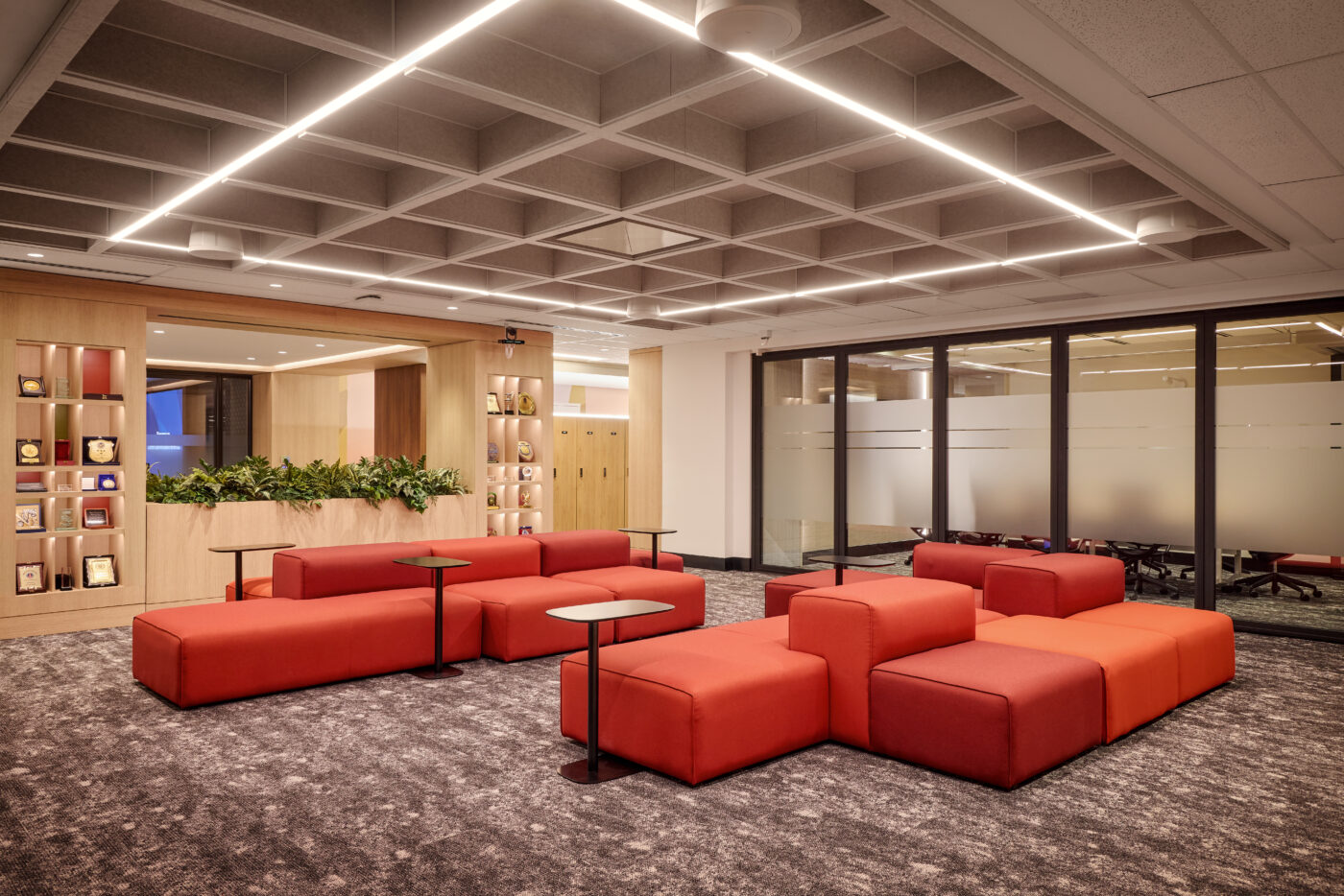 Lounge area featuring large modular seating units in bright red tones, and above is a square patterned detail on the ceiling with a linear LED light in a large square shape