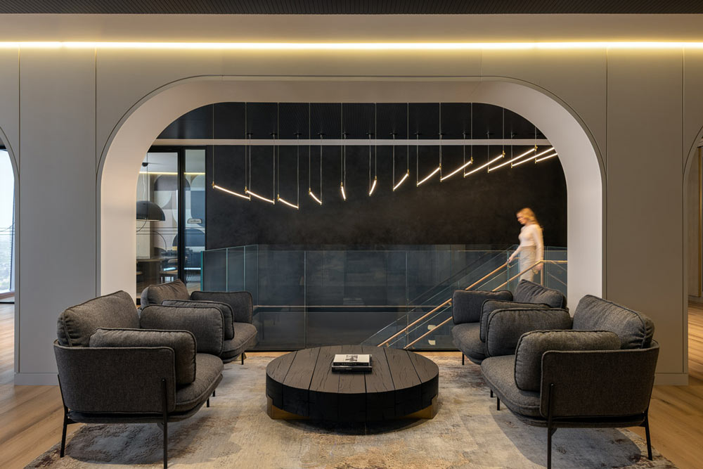An arch separates the stair case in the background from the lounge area in the foreground. The linear light fixture made up of multiple thin rods hangs above the staircase.