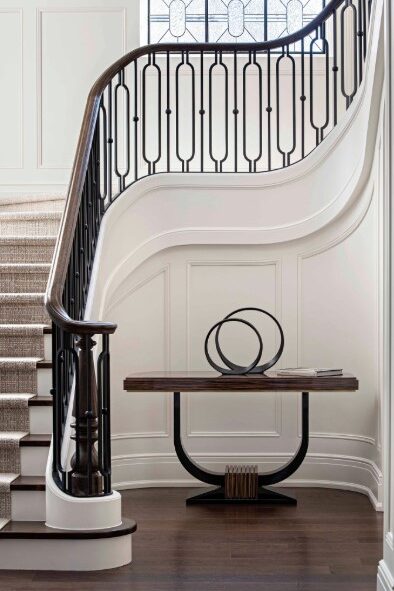 Stair hall featuring a beautiful contemporary design on the railing in black metal and wood that curves up the stairs, and is in perfect contrast to the white wainscoted walls.