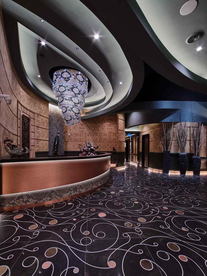 multi-tiered organically flowing bulkheads and a tall chandelier above the large copper encased curved reception desk. Custom designed and fabricated black ceramic tile floor, with free-flowing curved inlays of brass and copper