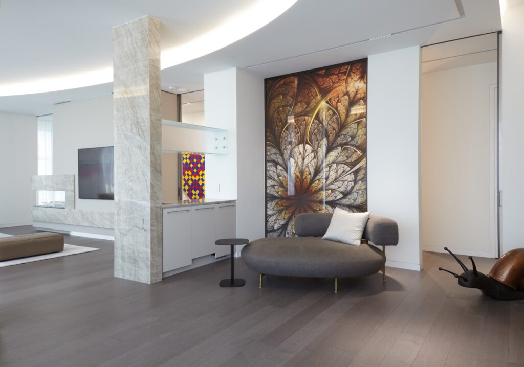 custom glass screen at the office elevator entrance, which includes a digitally printed image on a large glass panel and sits between the office and the private elevator. In front of the screen is a lounge chait a side table, and to the left of this lounge area is a large visiotrs' living room area