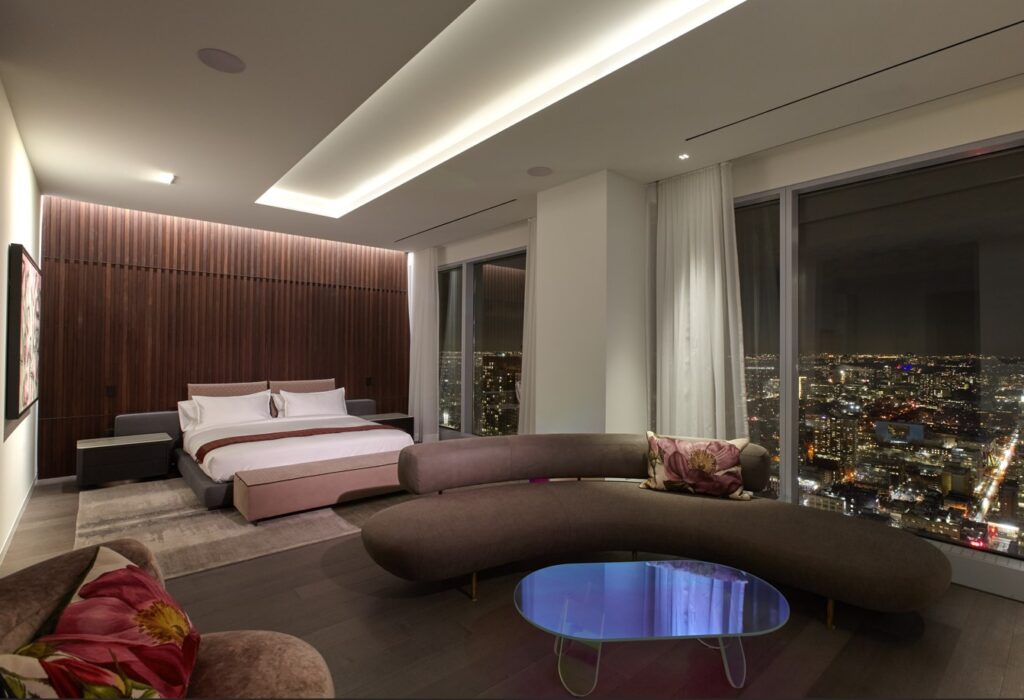 Moody and spacious bedroom in earthy dark tones, against the city skyline visible throught the floor to ceiling windows
