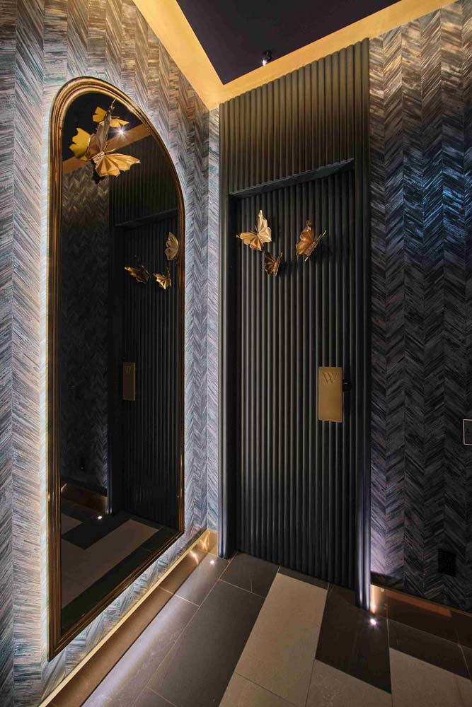 Black door in vertical slats next to an arched glass door, both are embellished with golden butterflies. The walls are covered in shimmering moss green mylar wallcovering