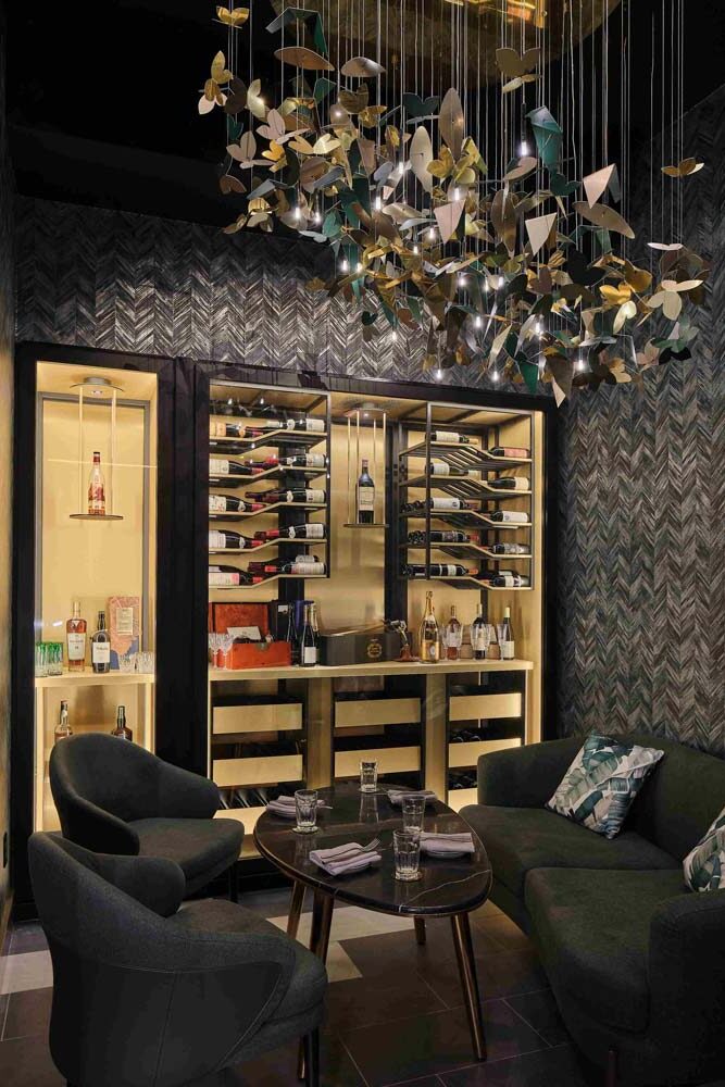 exclusive premium wine and spirits lounge. A custom wood open display case flanks the soft lounge seating only up to four patrons. A scaled down butterfly and leaves lighting fixture hovers above