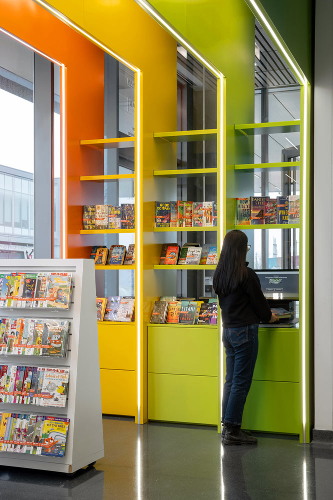 A person standing by the colourful niches containing shelves for book collections