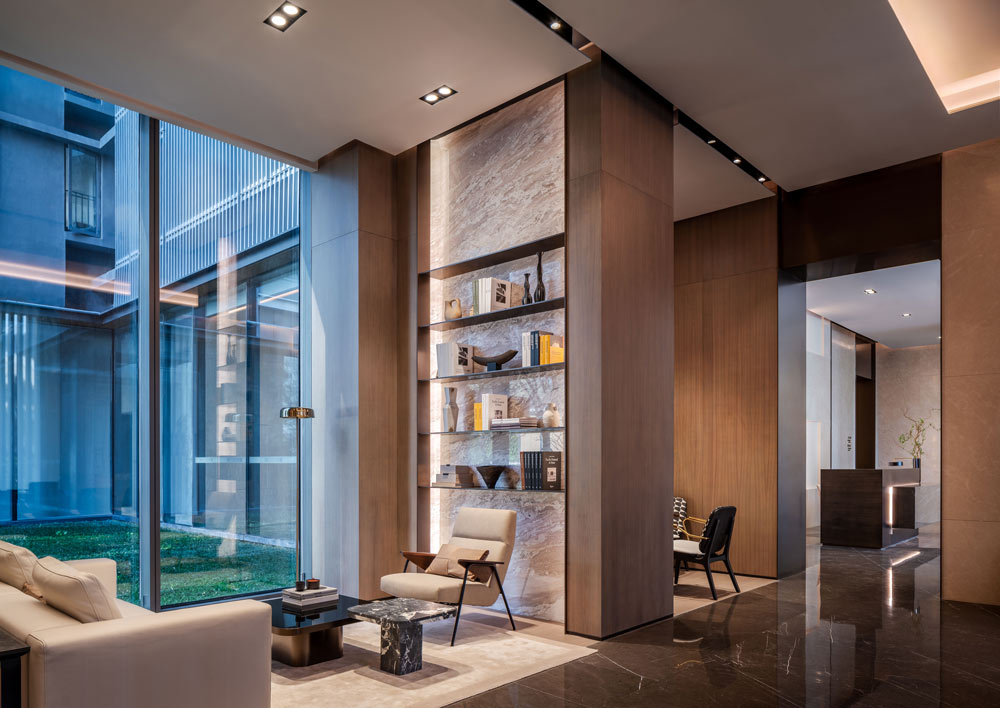 Book bar in the lobby area, with a lot of wood paneling around modern book shelves and lounge seating next to a large floor to ceiling window looking into the court yard