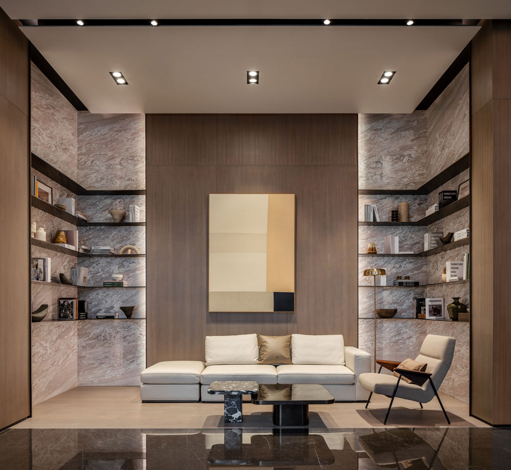 Book bar in the lobby area, with wall shelving full of books and decor items against a marble wall. In the centre of the space is a wood paneled wall with hanging artwork