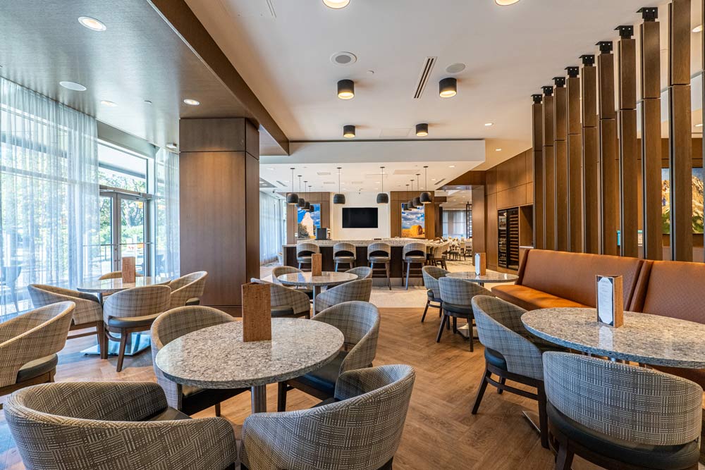 Lounge and bar area in earthy warm colour scheme, with small round tables and comfortable stylish chairs, and a lot of wood finishes and detailing throughout.