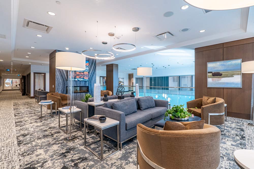 Another lounge area with lots of comfortable seating in neutral and warm earthy tones, lots of light and a large pool is visible right behind in the background