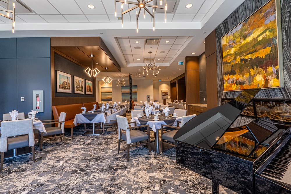 The formal dining room features linen-clad tables and candlelight, beautiful modern light fixtures above, and a concert piano is visibl in the corner of the photo.