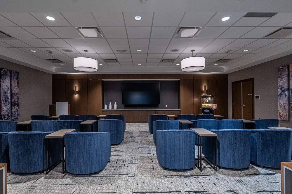 A spacious movie theatre room with blue lounge chairs placed in front of a very large TV hanging on the wall.