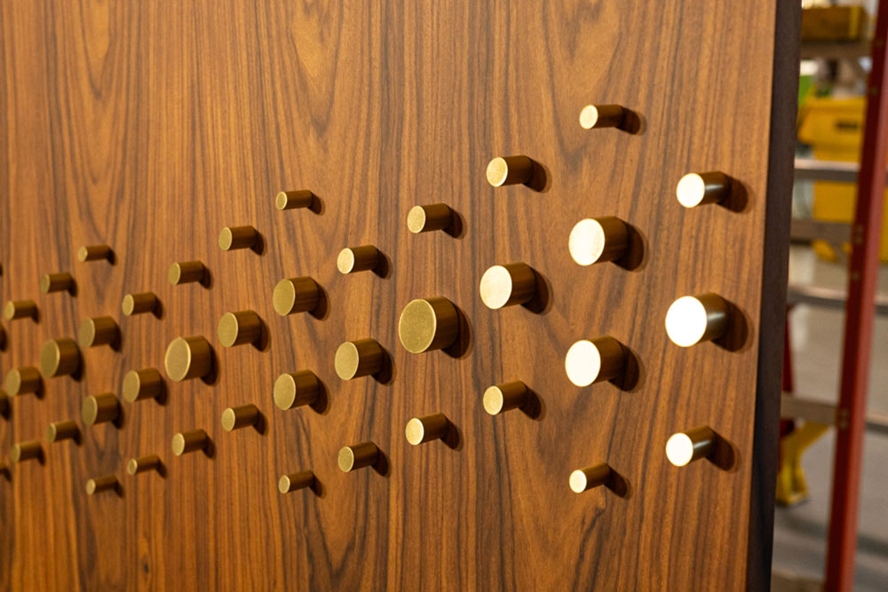 A close up  of the brass pegs on a wooden panel that suggest Braille with which impaired users can interact with