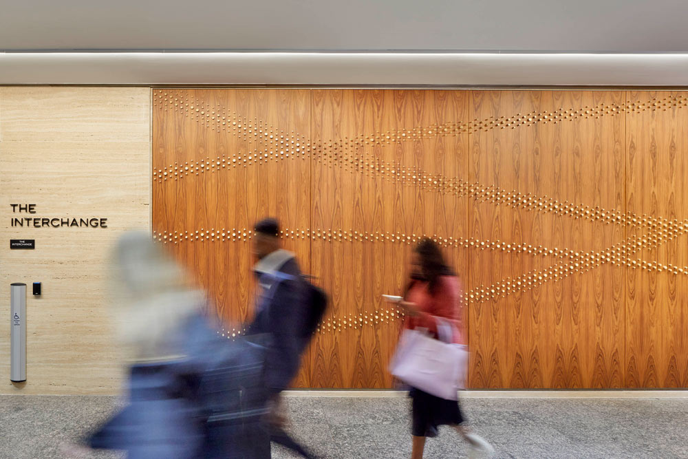 A frontal view of the mural, with people walking in front of it. The brass pegs create a wavy line pattern across the wooden wall paneling 