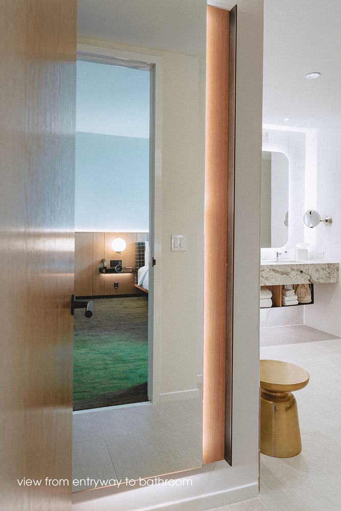 A view from the entryway into the bathroom, and a reflection of the bedroom in the tall wall mirror in the bathroom